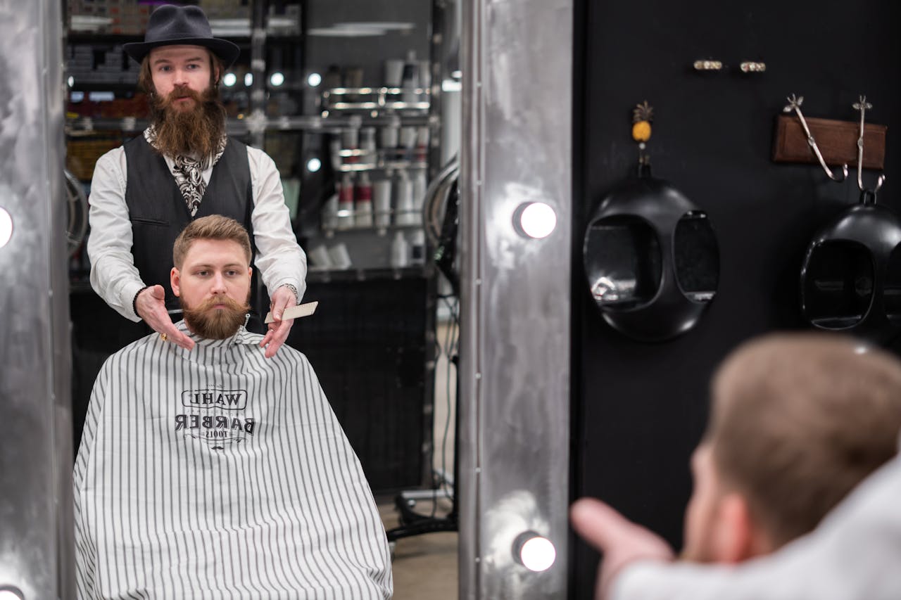 A bearded barber grooming a client's beard in a contemporary barbershop.