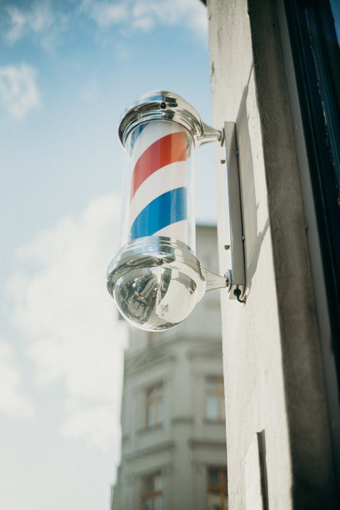 Vintage barber pole with red, white, and blue stripes outside a barbershop.